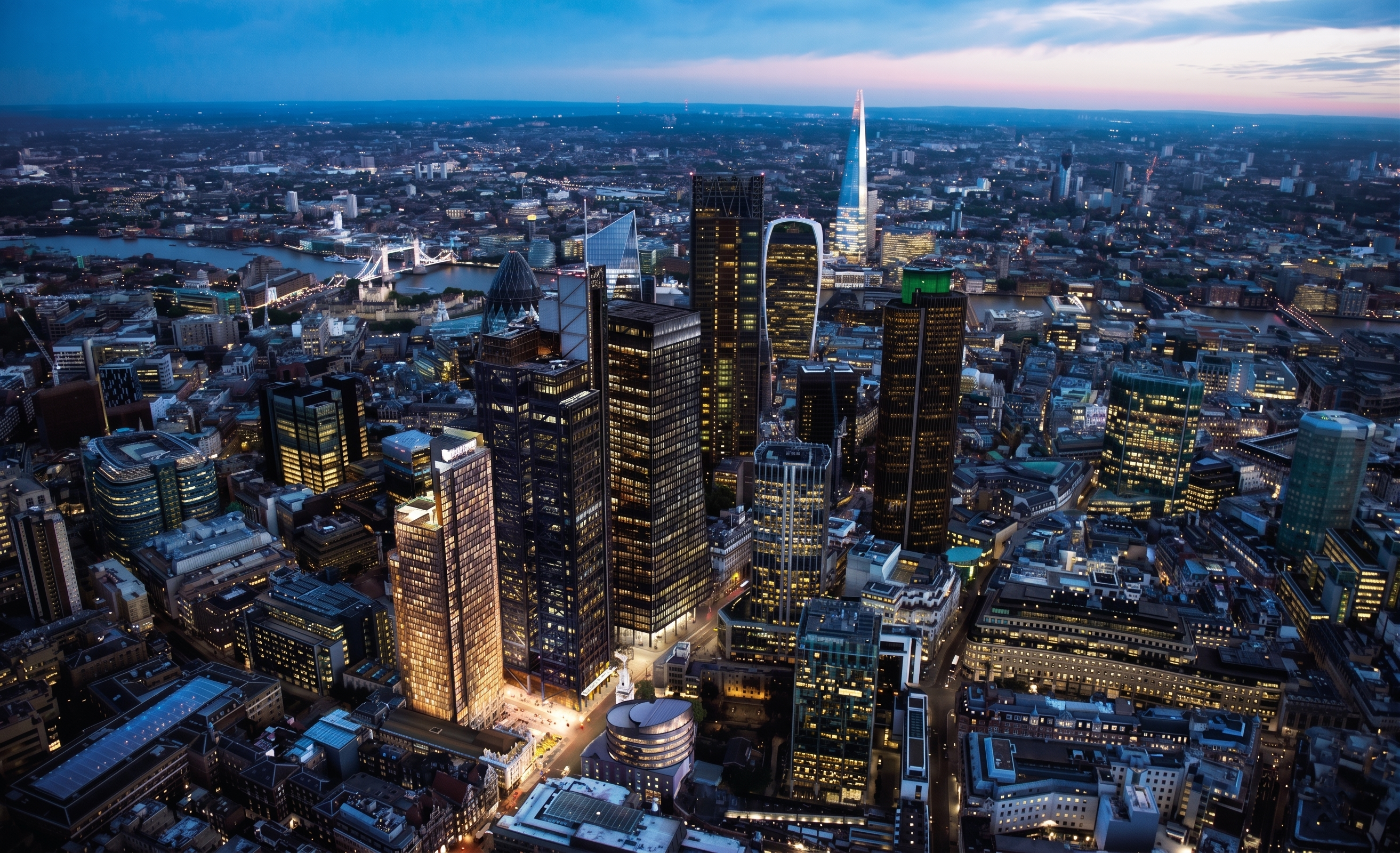 Aerial view of the City of London at dusk, with The Shard and Tower Bridge on the horizon